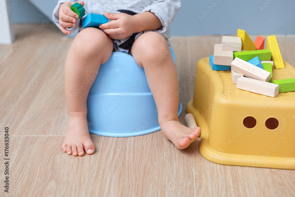 Closeup of legs of cute little Asian 18 months old toddler baby boy child sitting on potty playing with wooden blocks toy