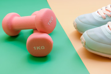 sport, healthy lifestyle and objects concept - close up sport shoes and dumbbells on green and orange background. Concept healthy lifestyle, sport and diet. Sport equipment. Copy space.