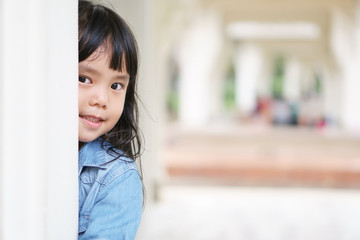 Wall Mural - Asian children cute or kid girl wear jeans for fashion and playing hide and seek with sneaked or dodge behind the post and smile white teeth in the pavilion at park garden on relax holiday with space