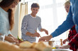© Seventyfour - Portrait of modern young man smiling happily while  preparing dinner with friends setting food on table for feasting celebration