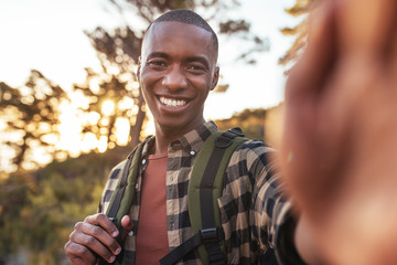 Wall Mural - Smiling young African man taking selfies while out hiking