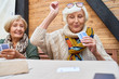 © Seventyfour - Portrait of cheerful seniors playing card game at lunch table on outdoor terrace, focus on two old women winning game