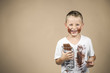 Little boy holds a bar of chocolate in his grin and has smudged clothes against colored background