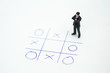 Business direction and planning concept. Businessman miniature figure standing and thinking on paper with OX (tic tac toe) board game.
