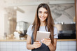 © Liubov Levytska - Young girl using a tablet computer running her cafe looking at camera happily smiling waiting for customers.