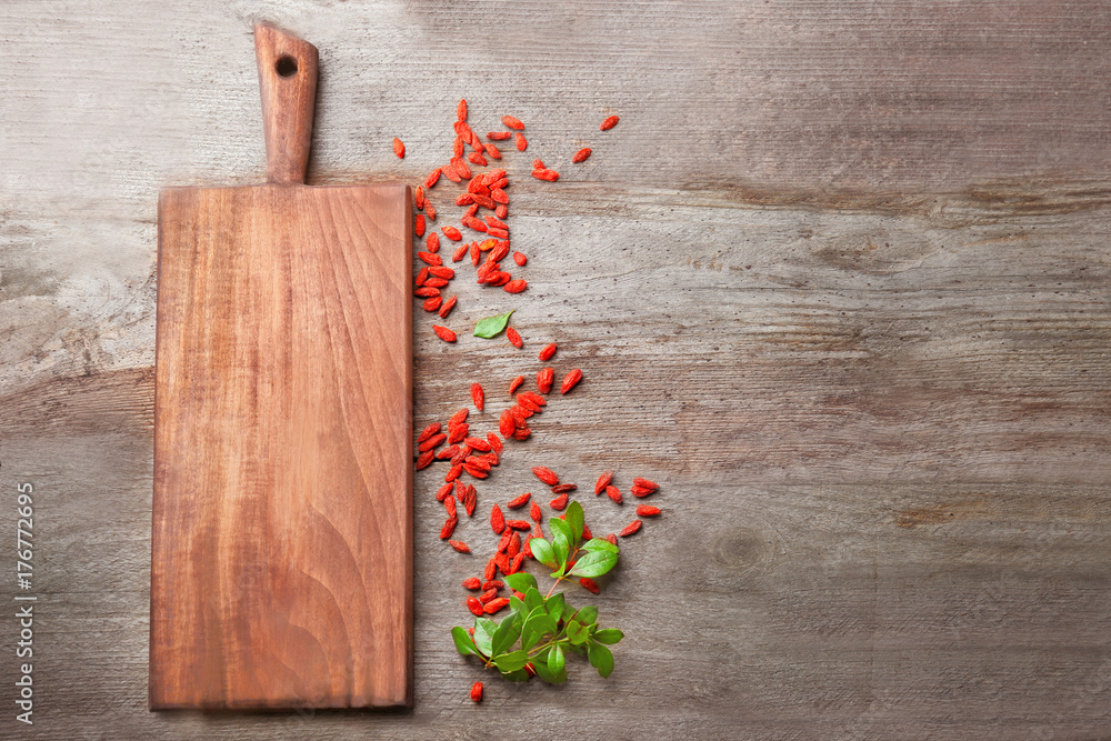 Board with red dried goji berries on wooden table