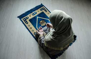 Wall Mural - Muslim woman praying for Allah muslim god at room near window. Hands of muslim woman on the carpet praying in traditional wearing clothes, Woman in Hijab, Carpet of Kaaba, Selective focus