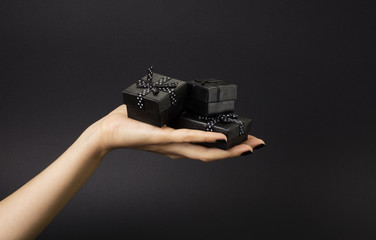 Female hand holding a three black gift boxes on a palm. Isolated on black background. Shallow depth photo.