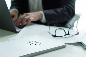 Lawyer working in office. Attorney writing a legal document with laptop computer. Glasses on table. Pile of paper with scale and justice symbol. Law firm and business concept.