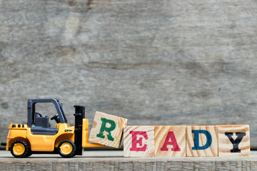 Wall Mural - Yellow plastic forklift hold letter R to complete word ready on wood background