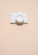 A White Camera On A Peach Colored Plain.