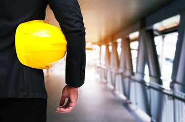 Wall Mural - back view of engineer and holding yellow safety helmet standing in front of steel roof frame for building construction background, industrial and business concept