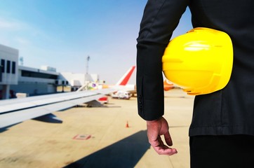 back view of engineer and holding yellow safety helmet standing with cargo on the plane at airport background, industrial, logistics, transportation and business concept