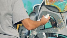 A Hand Shakes A Paint Can Near A Graffiti Wall. 