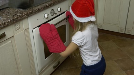 track slide shot. young girl claps hands and check cookies in oven. girl bakes gingerbread cookie. g