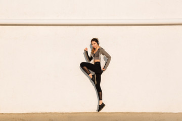 Wall Mural - Full length photo of young sport woman jumping near white wall