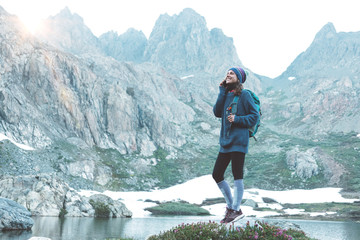 young happy traveling woman with backpack, hat standing on rock and chating on mobile phone in the s