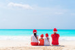Happy beautiful family in red Santa hats on a tropical beach celebrating Christmas