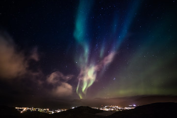 aurora borealis with shining stars on the sky over the mountains and highlighted city, nuuk, greenla