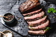 © jarvna - Sliced grilled roast beef with fork for meat on wooden cutting board. Black background. Top view.