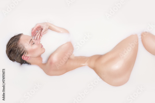 Fotografie, Obraz Beautiful young sexy girl with dark hair wet, natural makeup, takes bath with milk tan perfect skin in romantic atmosphere, beauty cosmetic salon and spa for woman