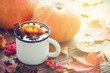 © chamillew - Mulled wine in enameled cup and pumpkins on wooden table with autumn leaves.