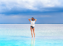 A Girl Stand On The Surface Of A Salt Lake At A Spa Resort. Young Woman On The Beach With White Sand Admires Beautiful Scenery Around