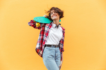 Sticker - Cheerful young teenage girl holding skateboard on her shoulders