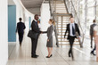 © Monkey Business - Businessman and woman shaking hands in a busy modern lobby