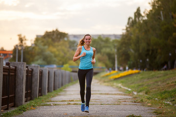 Young beautiful woman running in park in the morning. Sporty girl jogging along embankment