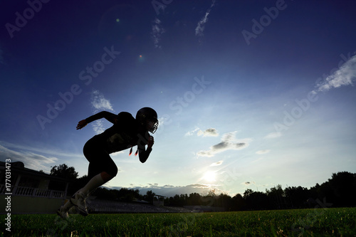 Plakat Amerykański piłkarz biegnie przez pole o zachodzie słońca.