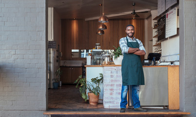 Wall Mural - Smiling African entrepreneur standing welcomingly in front of his cafe