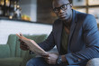 © jacoblund/Stocksy - Young African businessman sitting at cafe with a newspaper