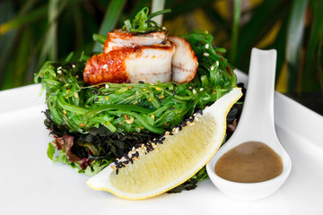 Salad with roasted fish and seaweed on a white table, Asian food