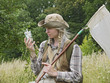 A girl entomologist in a field near a forest. Young woman with two plaits, in a hat, dressed in country style holds an insect net and a killing bottle. A student summer field period in the university.