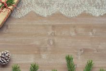 Christmas Background Gift In Kraft Paper Tied With Twine Adorned With Spruce Branch, Lace On  Old Boards And Cedar Cones