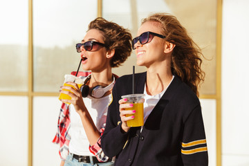 Wall Mural - Two smiling teenage girls in sunglasses drinking orange juice