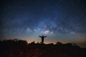 Landscape with milky way galaxy, Starry night sky with stars and silhouette of a standing sporty man with raised up arms on high mountain.