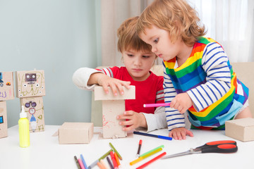 two little children together in creativity of the house. Happy kid makes the robot from cardboard boxes. Children's creativity.