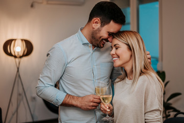 Wall Mural - Lovely couple drinking wine while hugging in their living room.