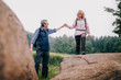 © Criene Images - Senior Man helping his wife climbing up a rock on hike
