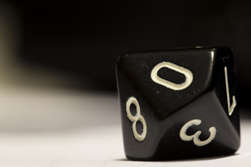 Macro shot of a black ten-sided die on side showing a zero