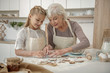 Cheerful grandchild learning to make pastry in kitchen