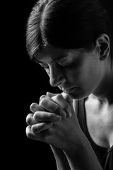 Wall Mural - Faithful woman praying, hands folded in worship to god with head down and eyes closed in religious fervor, on a black background. Concept for religion, faith, prayer and spirituality.
