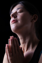 Wall Mural - Happy faithful woman praying and smiling in happiness, bliss and peace, feeling inspired with the presence of god and his grace. Hands folded in worship, head up, eyes closed, black background