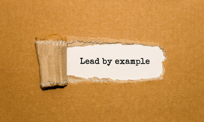 the text lead by example appearing behind torn brown paper