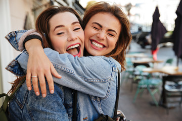 close-up photo of laughing woman friends hugging each other on city street