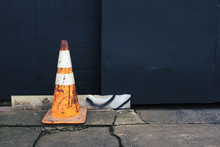 Traffic Cone On Cracked Urban Sidewalk, Painted Wall In Background