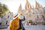 Fototapeta  - Young woman tourist photographing with phone famous saint Eulalia church during the morning light in Barcelona city