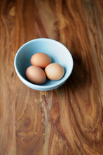 Three Brown Eggs In A Blue Bowl On A Wood Table